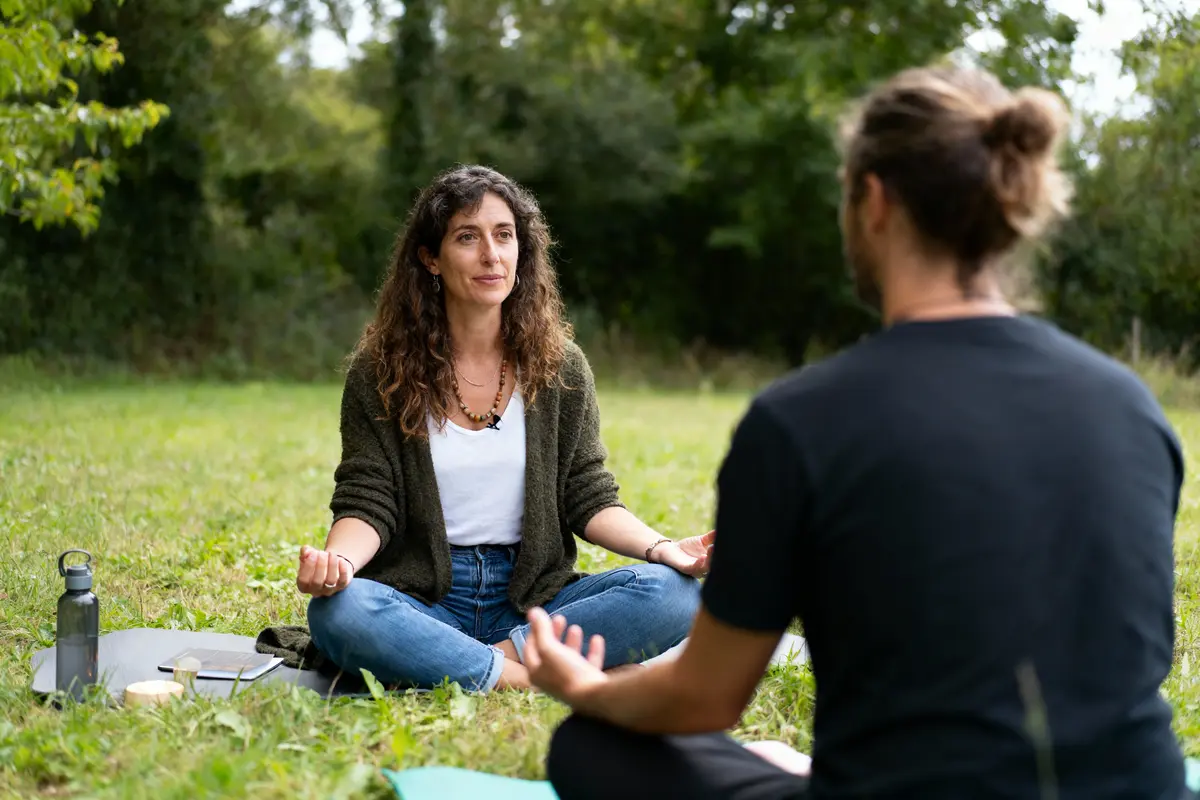 Personnes méditant dans un parc, assises en tailleur, discutant en plein air, entourées de verdure.