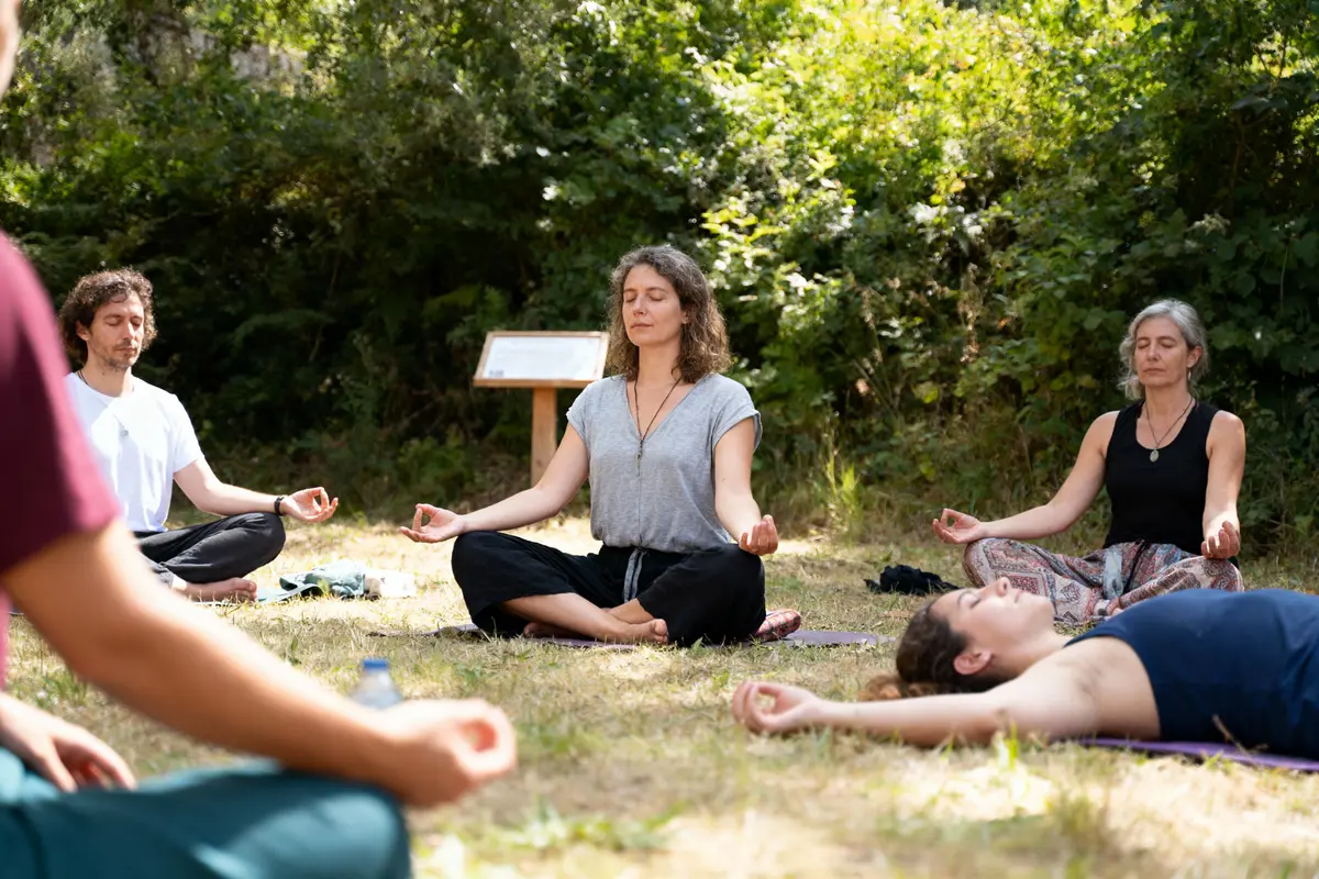 Personnes méditant en cercle dans un cadre naturel, herbe et arbres en arrière-plan, atmosphère paisible et relaxante.