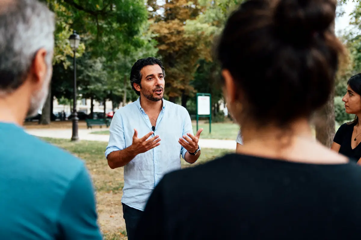 Homme parlant en plein air avec plusieurs personnes, environnement verdoyant, scène de communication en groupe.