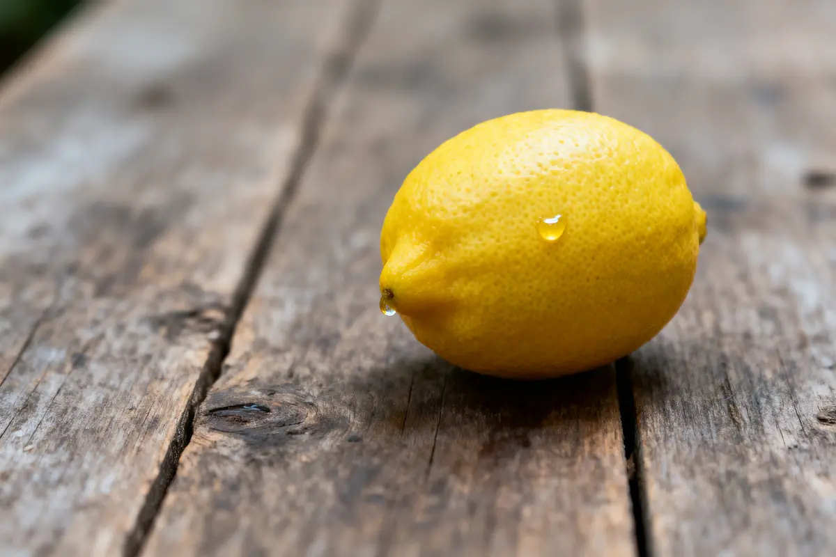 Citron jaune avec goutte d'eau sur table en bois brut, éclairage naturel.