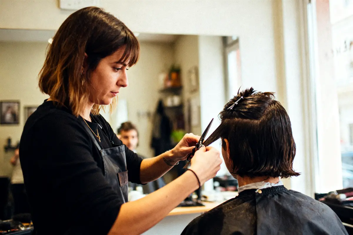 Coiffeuse coupant les cheveux d'une cliente dans un salon, lumière naturelle, ambiance professionnelle et élégante.