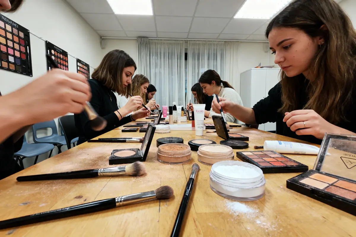 Personnes appliquant du maquillage autour d'une table avec palettes et pinceaux, dans une salle bien éclairée.