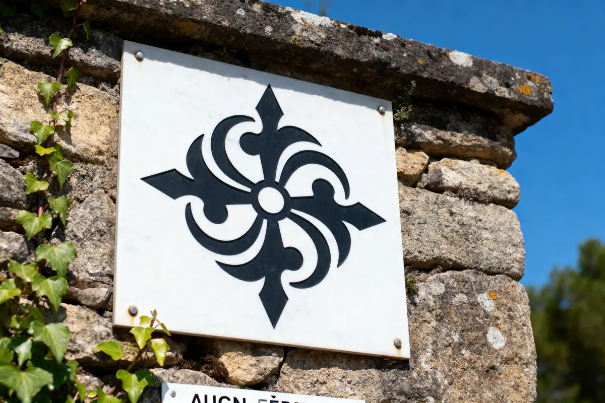 Panneau mural en pierre, symbole noir floral sur fond blanc, lierre grimpant, ciel bleu clair.