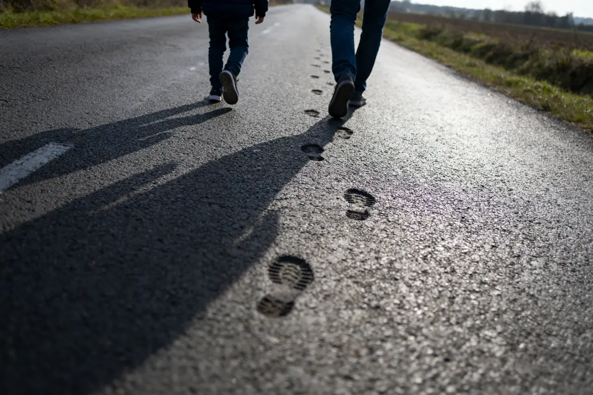 Deux personnes marchant sur une route, ombres longues, empreintes visibles sur le sol ensoleillé.