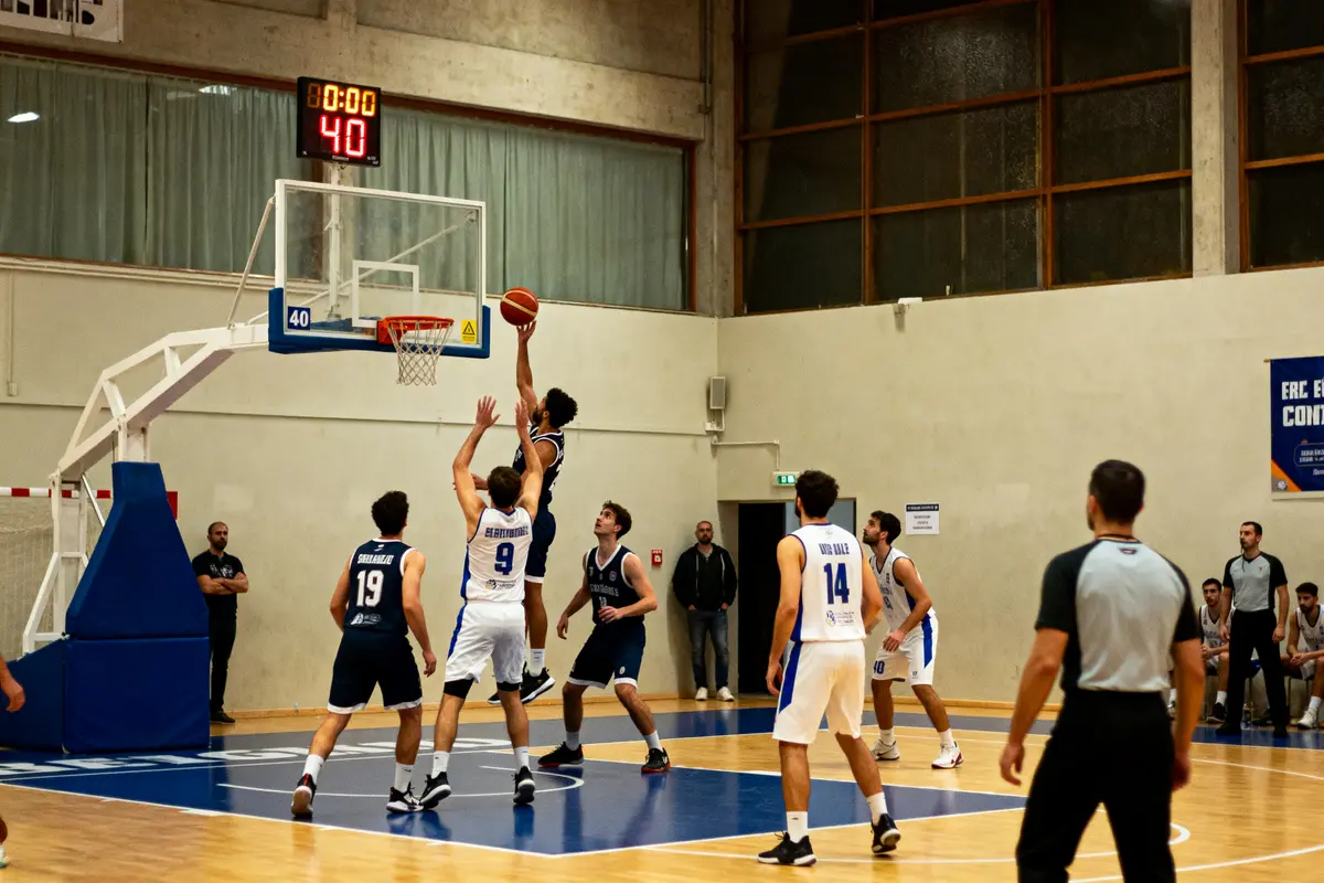 Match de basketball en salle, joueur effectuant un tir sous le panier, arbitre observant.